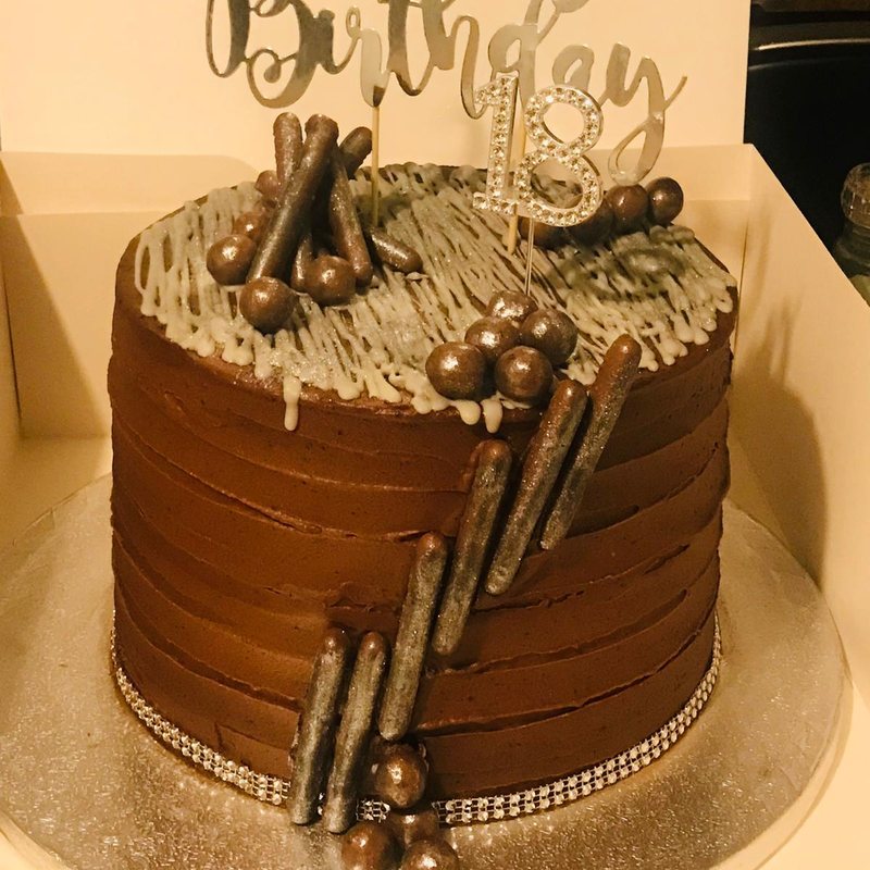 A tall chocolate birthday cake with a gold drip, chocolate cigarillos and gold pearls