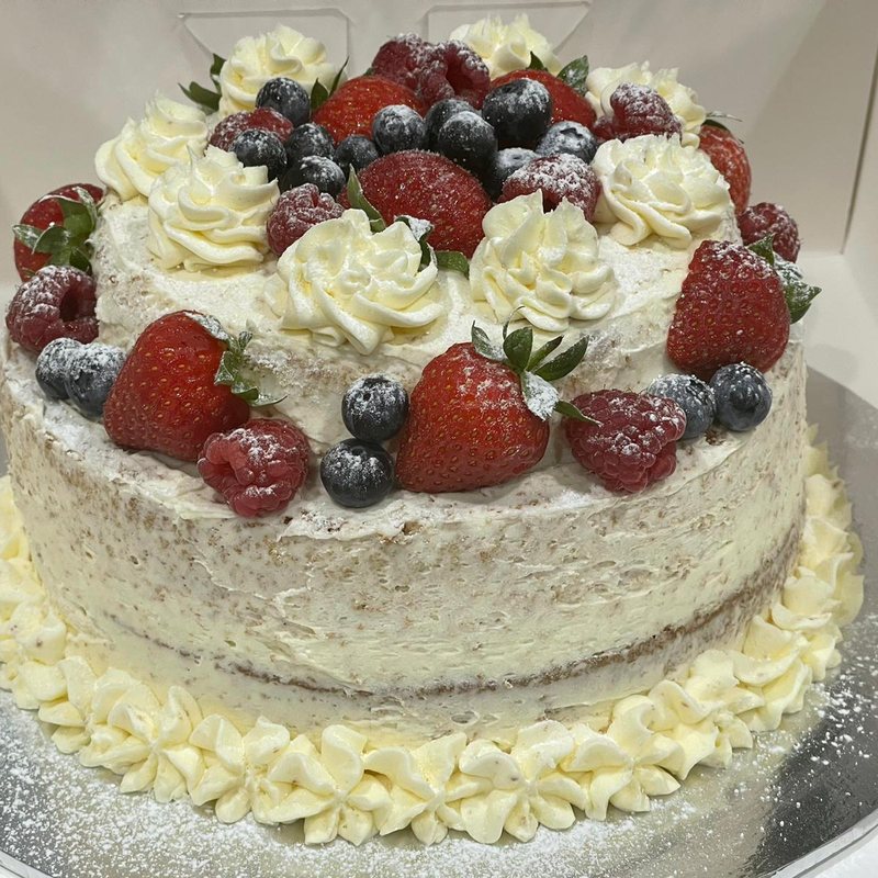 A two tier white celebration cake covered in piped cream, strawberries, blueberries and blackberries, baked by the Kongwa family in Medway