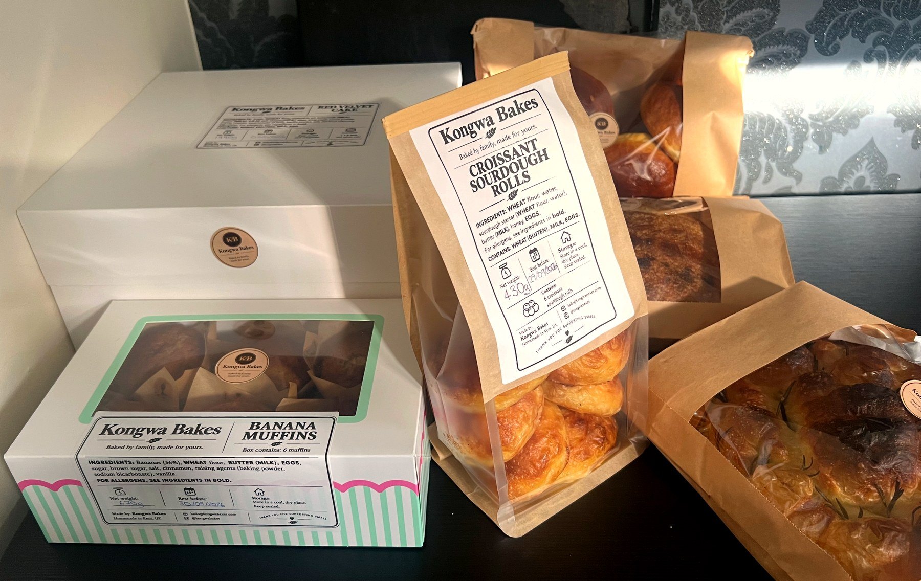 A Kongwa Bakes order boxed and bagged ready to go out, croissant sourdough rolls and banana muffins in labelled kraft packaging